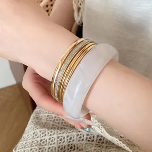 Close-up view of a luxury five-piece resin and gold metal bangle set worn on a wrist.
