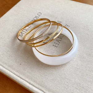 Detail of five-piece set with white resin bangle and gold-plated metal bracelets
