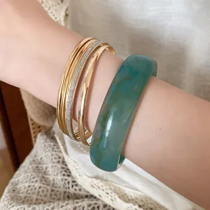 Detail view of 5-piece set featuring a green resin bangle and gold metal bracelets