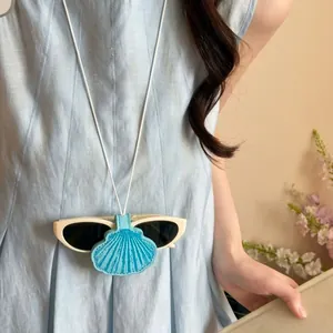 Detailaufnahme der Muschel-Leder-Magnet-Brillenclip-Halskette an einem hellblauen Kleid