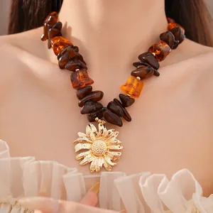 Dettaglio di una collana di perle in resina ambra con grande ciondolo a girasole d'oro.