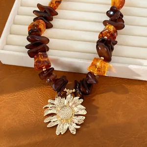 Dettaglio di perle in resina ambra e pendente girasole dorato su vassoio portagioie.