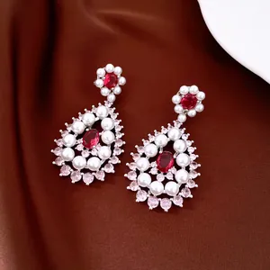 Detail shot of teardrop pearl earrings with red zircon accents on brown silk background
