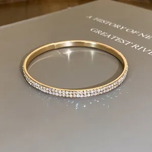 Close-up van een goudkleurige armband met dubbele rij strass-steentjes op grijs