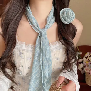 Detail eines blauen karierten Chiffon-Schals mit passender Rosen-Haarspange am Modell.