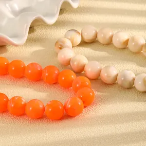 Makrodetail einer handgefertigten Halskette mit leuchtend orangen und beige Perlen.