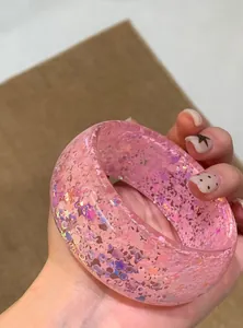 Macro detail view of chunky pink acrylic bangle with iridescent holographic glitter.