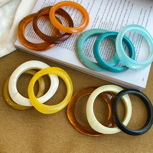 Set bunter, unregelmäßiger, geometrischer Acryl-Armreifen auf Vintage-Buch-Hintergrund