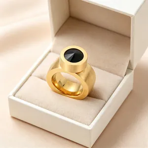 Gros plan d'une bague dorée avec une pierre noire dans un écrin à bijoux de couleur crème.