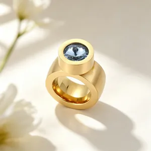 Vue rapprochée d'une bague large dorée avec un serti clos en pierre bleue facettée