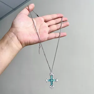 Gros plan d'un collier avec pendentif croix en zircon vert menthe tenu dans la main