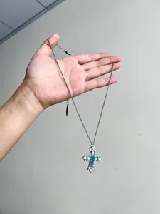 Vue détaillée d'un collier avec pendentif croix en zircon vert menthe tenu à la main