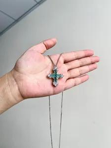 Vue détaillée d'un collier pendentif croix en zircon vert menthe tenu à la main
