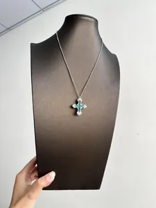 Gros plan du collier croix en argent orné de pierres de zircone vert menthe et claires.