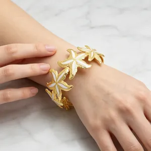 Elegantes goldfarbenes Seestern-Manschettenarmband mit weißem Emaille-Detail am Handgelenk