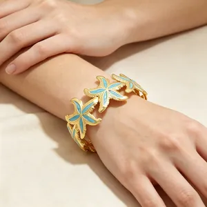 Detailansicht des eleganten goldenen Emaille-Seestern-Armreifs am Handgelenk einer Frau