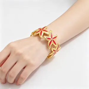 Elegantes Modell trägt ein goldenes Seestern-Emaille-Armband mit roten Details