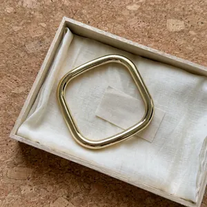 Primer plano detallado de un brazalete cuadrado dorado pulido en una caja de madera