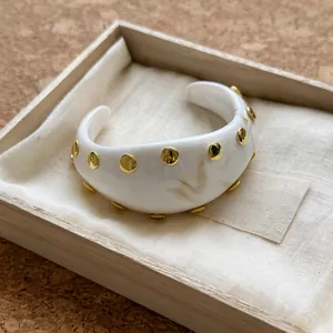 Vista detallada de un brazalete de resina blanca con tachuelas redondas en tono dorado.
