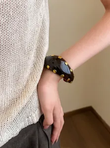 Brazalete grueso de resina marrón oscuro con tachuelas doradas en el brazo de modelo