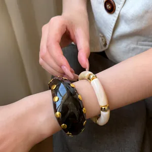 Vue rapprochée d'une manchette en résine à clous et bracelet à segments crème