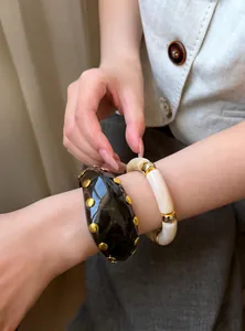Detalle de primer plano de elegantes pulseras de resina con tachuelas doradas en la muñeca.