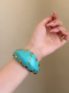 Primer plano de un brazalete de resina turquesa con tachuelas doradas en la muñeca