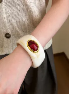 Detalle de brazalete retro de resina crema con gema roja en la muñeca de modelo.