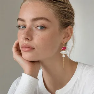 Close-up of model wearing long gold tassel earrings with red acrylic and pearls