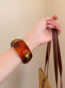 Detalle de un brazalete geométrico de resina ámbar con motivos de rayos de sol dorados