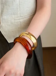 Primer plano de un brazalete de metal dorado y una pulsera de resina ámbar veteada