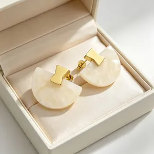 Détail de boucles d'oreilles en résine en forme d'éventail crème avec accents dorés en boîte