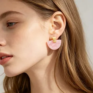 Gros plan de boucles d'oreilles en résine rose en forme d'éventail dorées