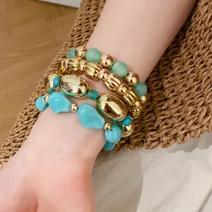 Primer plano de elegantes pulseras boho en capas con cuentas doradas y turquesas en la muñeca.