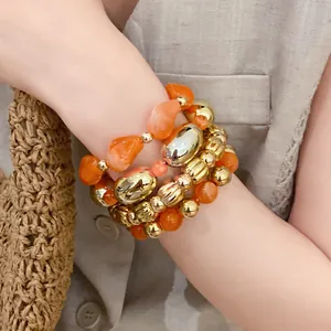 Primer plano de un conjunto de pulseras elásticas de acrílico naranja y cuentas doradas