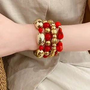 Pulseras apiladas de cuentas acrílicas geométricas irregulares rojas y doradas.
