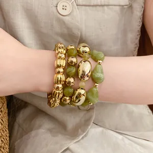Detalle de un conjunto de pulseras elásticas de acrílico verde y cuentas doradas en la muñeca