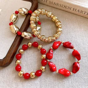 Primer plano de un conjunto de pulseras elásticas geométricas de acrílico en rojo y dorado.