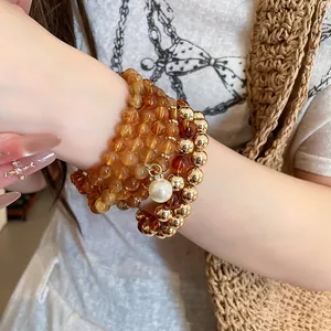 Close-up detail of a multi-layered amber and gold beaded bracelet set featuring a pearl charm