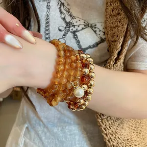 Close-up detail of a luxury beaded bracelet set featuring amber beads and a pearl charm.