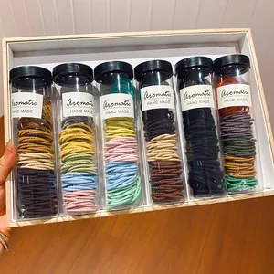 Detail van kleurrijke elastische haarelastiekjes in zes transparante buizen met zwarte doppen.
