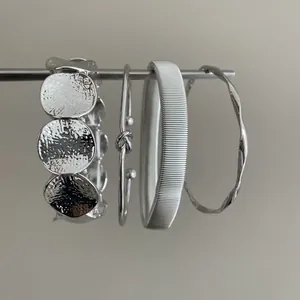 Set di 4 braccialetti geometrici color argento con disegni martellati e a nodo.