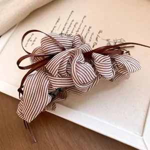 Close-up detail of a brown striped pleated fabric hair claw clip with satin ribbon tassel