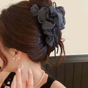Detailed side view showing a black and white striped ribbon bow hair claw with tassels