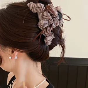Detailed view of a brown and white striped fabric bow hair claw clip worn by a model