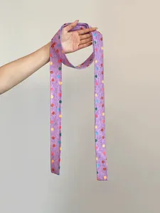 Accesorio largo de poliéster morado con lunares de colores sujeto por la mano