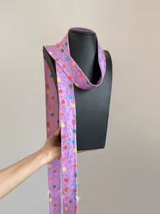 Detalle de una bufanda larga de poliéster morada con lunares de colores en un maniquí negro