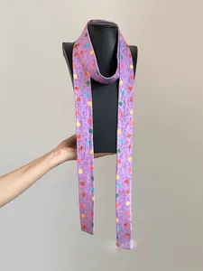 Detalle de una bufanda larga de poliéster morada con lunares de colores vibrantes.