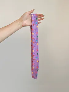 Primer plano de una bufanda larga morada con lunares de poliéster en la mano.