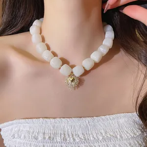 Close-up of white resin square beaded necklace with golden heart sunburst pendant.